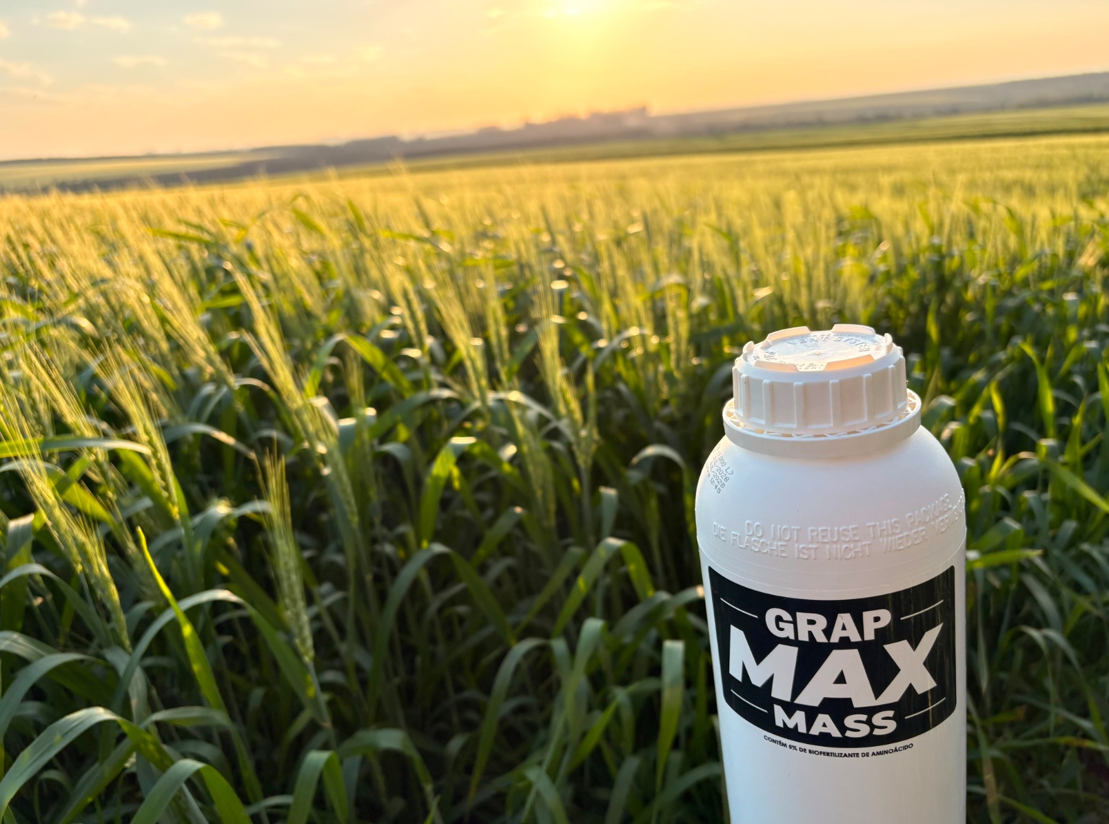 Embalagem de GRAP MAX MASS em primeiro plano diante de uma lavoura ao pôr do sol